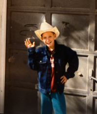 Young Eric wearing a cowboy hat and waving outside